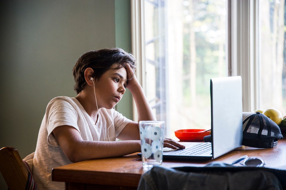 Eleven year-old boy at home using a laptop at a kitchen table